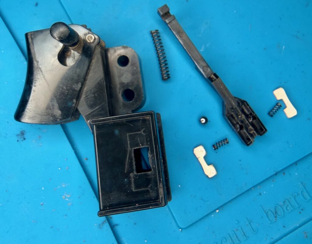 Components of the RB1 switch: The frame, including trigger and hold button; a sled which the trigger pulls against a large spring, over a ball bearing, and presses through the two smaller sprints, the metal contacts.